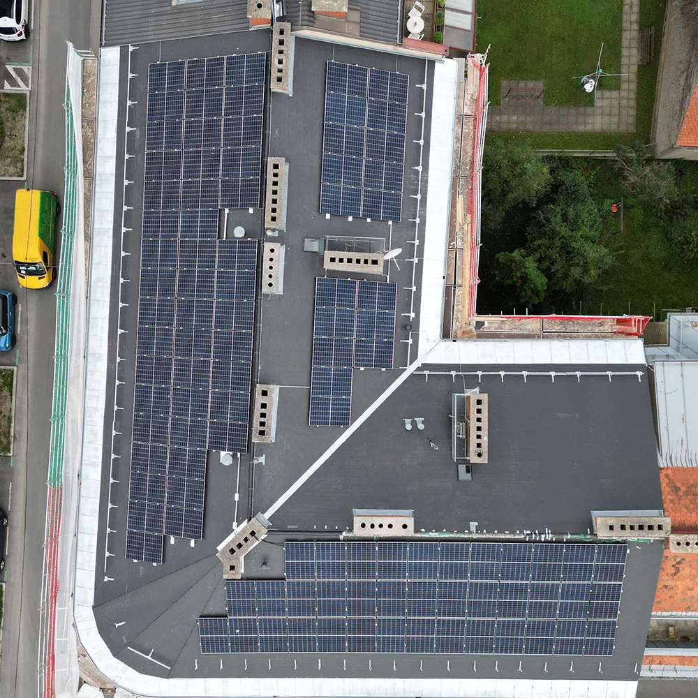 Luftaufnahme der Photovoltaikanlage auf dem Dach der GEA Hermann-Bahr-Gasse in Graz. Die Solaranlage hat eine Leistung von 47,3 kWp und versorgt 26 Wohneinheiten. Die PV-Module sind auf dem Flachdach eines Wohngebäudes einer Wohnungsgemeinschaft (WEG) installiert. Das Gebäude befindet sich in einer urbanen Umgebung mit angrenzenden Wohnhäusern, Straßen und Grünflächen.